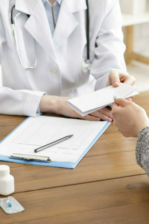 Prescription for medication and examination by doctor. Adult woman therapist gives paper to patient at workplace with tablet and jars of pills in office interior, cropped, close up, copy space